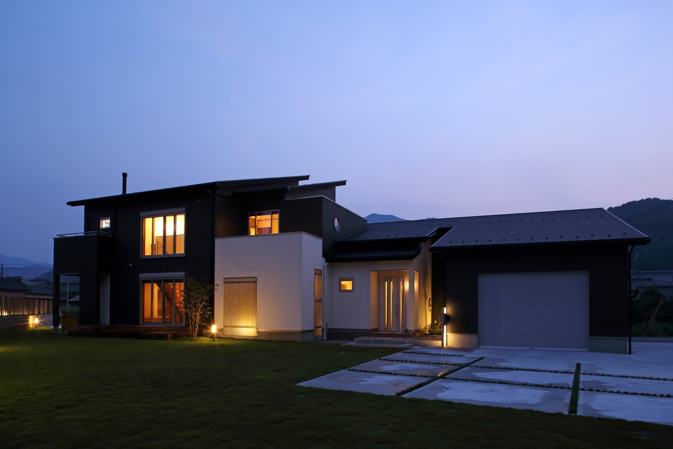 夕景の中に美しく浮かび上がる、ビルトインガレージを備えた和モダン住宅。黒と白のコントラストを活かした外観デザインと、水平ラインを強調した建築構成が、ホテルライクな高級感と落ち着きを演出。大開口から漏れる暖かな灯りと、広々とした芝生の庭が、家族時間を豊かに包み込む。車好きのライフスタイルに寄り添うガレージハウスとして、愛車を美しく納めながら、暮らしの質も高める設計。奈良県で和モダン住宅・デザイナーズ住宅・高級注文住宅・ビルトインガレージのある家を検討している人へ向けた建築事例。